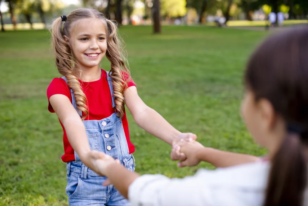 Empatia para criança - duas meninas de mãos dadas e uma delas sorrindo.