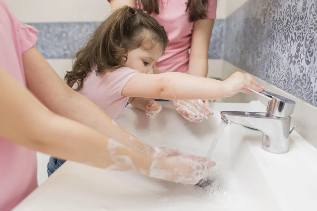 Hábitos de Higiene: crianças lavando as mãos, em uma pia grande.