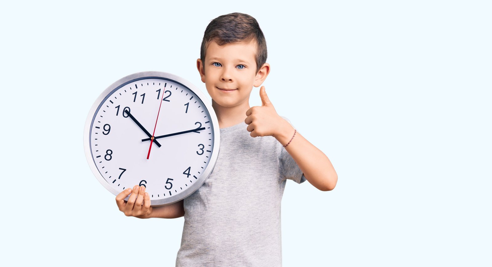 Menino segurando um relógio e fazendo o sinal de positivo para a rotina infantil.