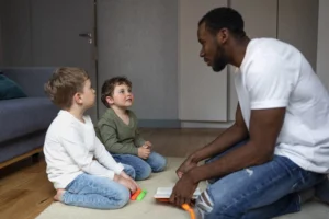 Conversar com as crianças de maneira respeitosa: homem de joelhos, olhando nos olhos de duas crianças e conversando com elas.