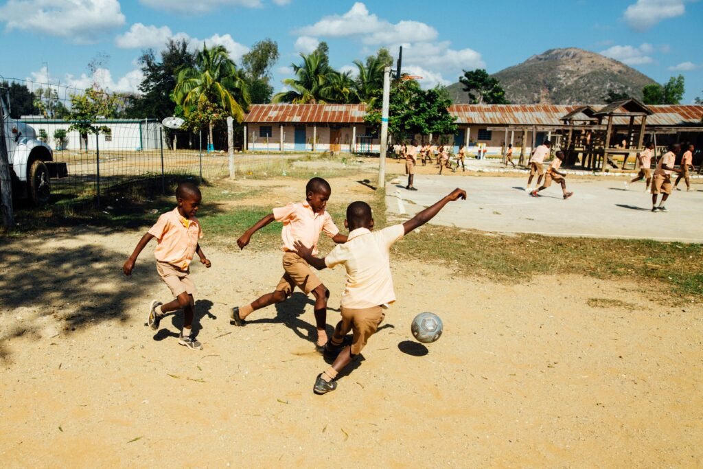 Crianças jogando futebol em um campo de areia trazendo a importância das brincadeiras para o desenvolvimento infantil.