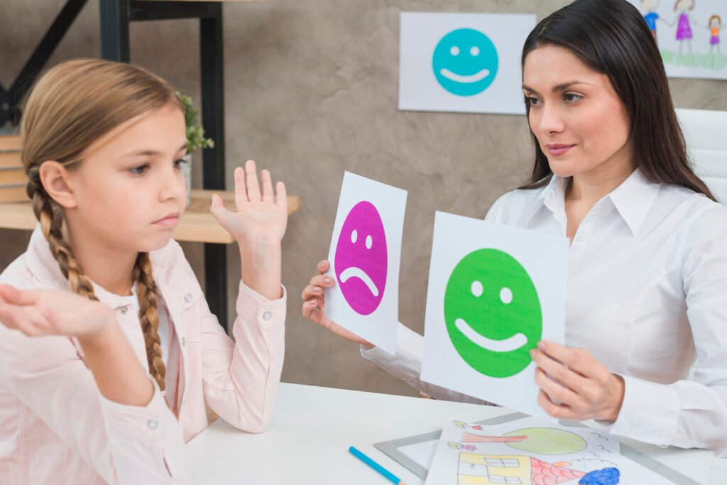 Saúde Emocional: uma mulher adulta mostrando placas com figura de triste e feliz para uma menina.