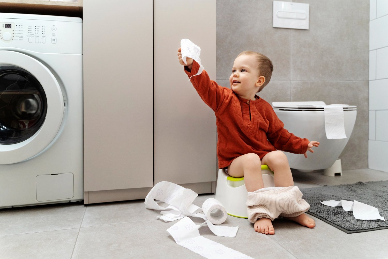 Menino sentado no vaso sanitário brincando com papel higiênico.