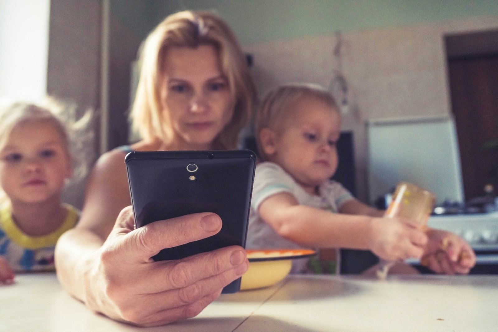 Mulher segurando um celular com dois filhos no colo. Desmistifique a criação dos filhos.